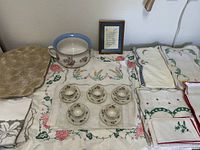 Overview photo of the set including linens, six cups with saucers, a chamber pot, and framed text