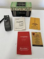 Vintage Keystone K-8 camera with original box and various manuals and guides laid out on a white surface.