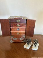 Photo showing the vintage wooden jewelry box with its two front doors open, revealing five drawers, alongside two small metal elephant bookends on white onyx bases.