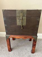 Full view of wooden storage chest on separate wooden stand showing brass corner trims and latch hardware