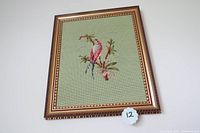 Framed needlepoint picture showing a bird perched on a branch with flowers on a green background. Gold frame with detailed beaded inner border.