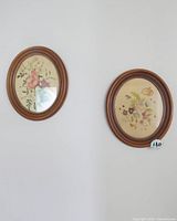 Two oval framed floral paintings on a white wall, showing overall appearance and size.