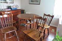 Photo showing round wooden dining table and 4 chairs including a captain's chair with arms.