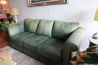 Front view of the forest green leather three-seater sofa placed in a living room, showing the seat cushions and pillows.