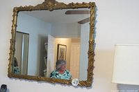 Full view of the antique square mirror mounted on a wall, showing the gold ornate frame and reflective surface.