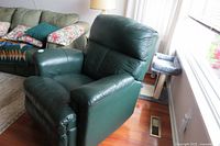 Side angle view of the green leather recliner chair showing padded armrests and seat cushion.