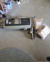Electrolux 2100 vacuum cleaner with hose outlet, control panel, wheels; one cleaning attachment wand; two unopened packs of vacuum bags in front on floor.