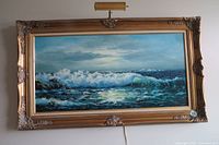 Full view of the framed seascape oil painting showing ocean waves under a cloudy sky and the ornate gold frame with attached lighting above.