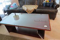Top view of rectangular coffee table with beveled glass top reflecting surrounding items, placed in front of a brown leather couch.