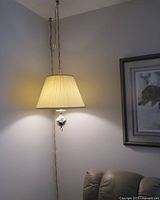 Hanging brass lamp on chain with pleated beige fabric shade lit and angled view