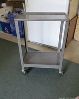 Full view of metal 2 tier utility cart on caster wheels on carpeted floor.