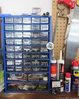 Front view of blue metal cabinet featuring numerous clear plastic drawers filled with various nuts, bolts, screws, washers and other small hardware items.