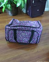 Full image of the Millennium carry on suitcase with purple snakeskin patterned fabric, black handles, and front zippered pocket, sitting on wooden floor.