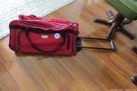 Full side view of red Protégé duffle bag with telescoping handle extended on hardwood floor
