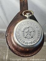 Pocket watch seated in leather holder; back cover with Cyrillic text and 1941-1945 wreath visible