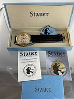 Watch in open Stauer box with manual and authenticity card visible