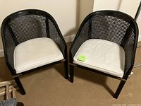 Front view of two matching black rattan-backed accent chairs with white cushions.