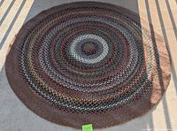 Top-down image of a large round braided area rug displayed flat, showing concentric ring colors and braided pattern.
