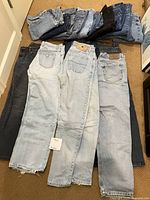 18 pairs of jeans laid out showing front and back with visible brand patches and different denim colors.
