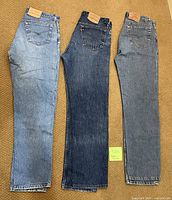Three pairs of Levi Strauss 501 button-fly jeans laid flat on carpet, showing side profiles.