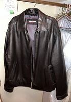 Front view of men's black leather jacket by Kirkland hanging on a hanger