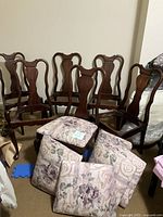 Group photo showing six wooden dining chairs with floral cushions placed in front. Cushions are detached or loosely placed in front of chairs.