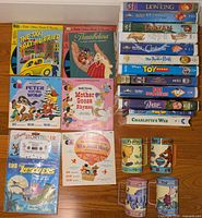 Photo of all items showing Disney VHS tapes stacked on the right, Little Golden Books with cassette records on the left, and Winnie the Pooh ceramic cups in front.