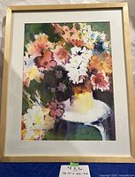 Full view of framed watercolor painting of colorful flowers in vase on white side table.