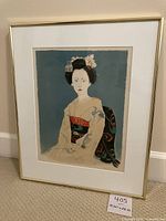 Framed geisha art print in gold frame leaning against wall.