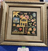 Framed needlepoint art showing the whole artwork including the golden ornate frame and linen matting.