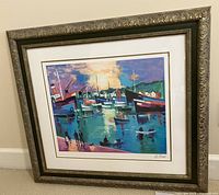 Frontal view of framed artwork showing colorful harbor scene with boats and sunset. Ornate gold-tone frame with cream and gold double matting. Signed at bottom right.