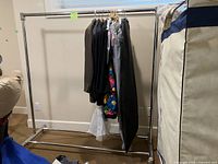 Full view of one assembled chrome clothes rack with hangers and clothes displayed, rack base and height visible.