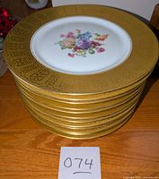 Stack of all 12 Heinrich & Co Selb Bavaria dinner plates showing gold leaf borders and floral centers.