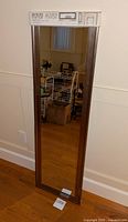 Front view of full-length over the door mirror with packaging intact, showing reflections of a room.