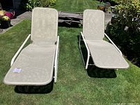 Two beige mesh Samsonite outdoor reclining chairs on grass with metal white frames, shown from a slight angle.