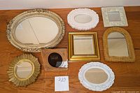 Seven small framed mirrors arranged on floor showing variety of frame styles and shapes.