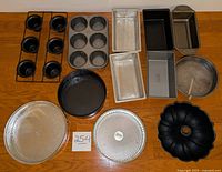 Overview of all baking pans displayed including springform, bundt, loaf pans, muffin tins, and round cake pans spread out on wooden surface