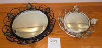 Both metal-framed concave mirrors with decorative leaf accents, placed on a wooden surface