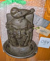 Front view of the wall-mounted bird bath displaying face, hands, and bird detail.