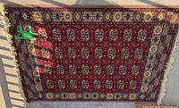 Top-down photo of large rectangular woven wool rug with red field and floral medallions, visible white fringes at ends, laid flat outside on concrete surface.