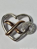 Heart-shaped silver pendant with an intertwined rose gold-tone infinity symbol and a diamond-accented small circle on the right side, clearly showing material and condition.