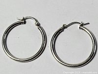 Pair of smooth, polished silver hoop earrings with hinged clasp closure, laid flat against white background.
