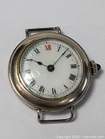 Full view of the antique men's wristwatch, showing porcelain dial with black Roman numerals and red 12, metal case, and blue gem on the crown.