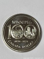 Obverse side of the 1974 Winnipeg Centennial Canada One Dollar Coin showing detailed city and historical images within the denomination.