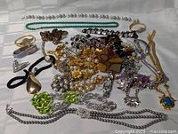 Photo of assorted vintage costume jewelry pieces spread out including necklaces, bracelets, brooches, and earrings in various metals and colors.