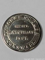 Front side of silver-colored round medallion showing inscription for St. John's Church Cornwall, Rev. H. Urquhart, and 1827 date.