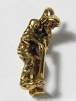 Close-up of gold-toned pewter golf player pendant charm showing front and side details, highlighting crouched golf putting pose.