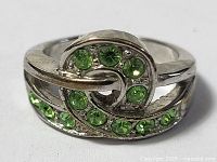 Close-up image of ladies silver ring showing green gemstones embedded in swirl design, highlighting the upper part and ring band detail.
