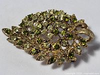 Top view of green stone brooch pin showing clustered round and marquise-cut stones with leaf and bow design