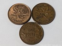 Front view of three older Canadian one cent coins from 1941, 1948, and 1920 with maple leaf design.